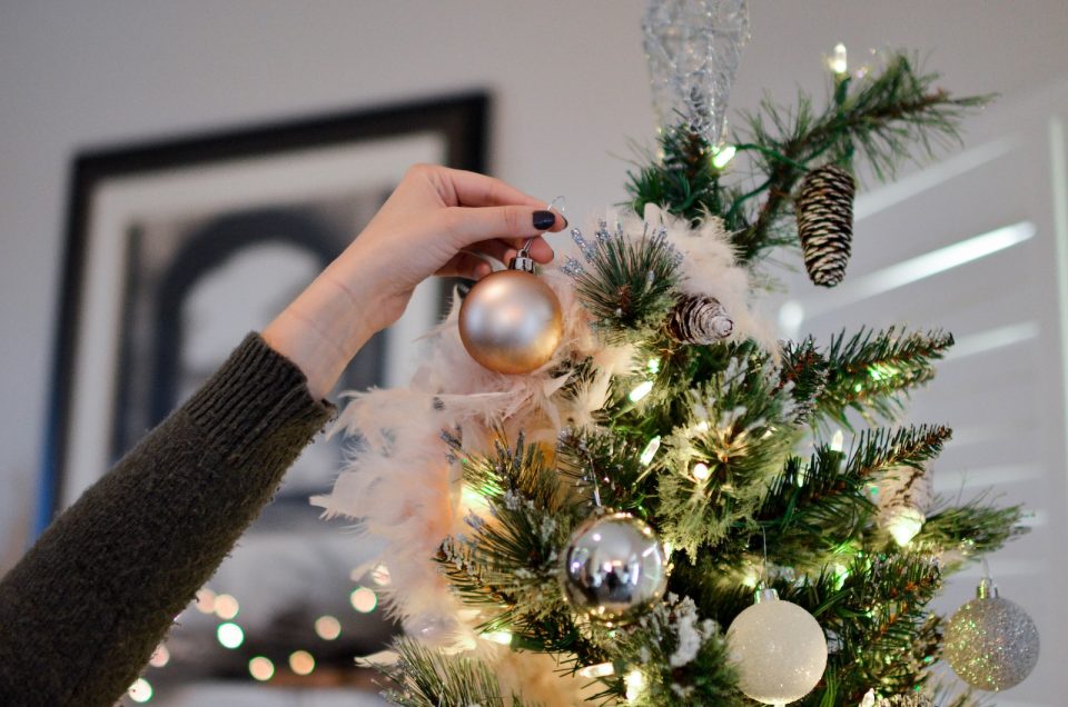person putting bauble on top of Christmas tree