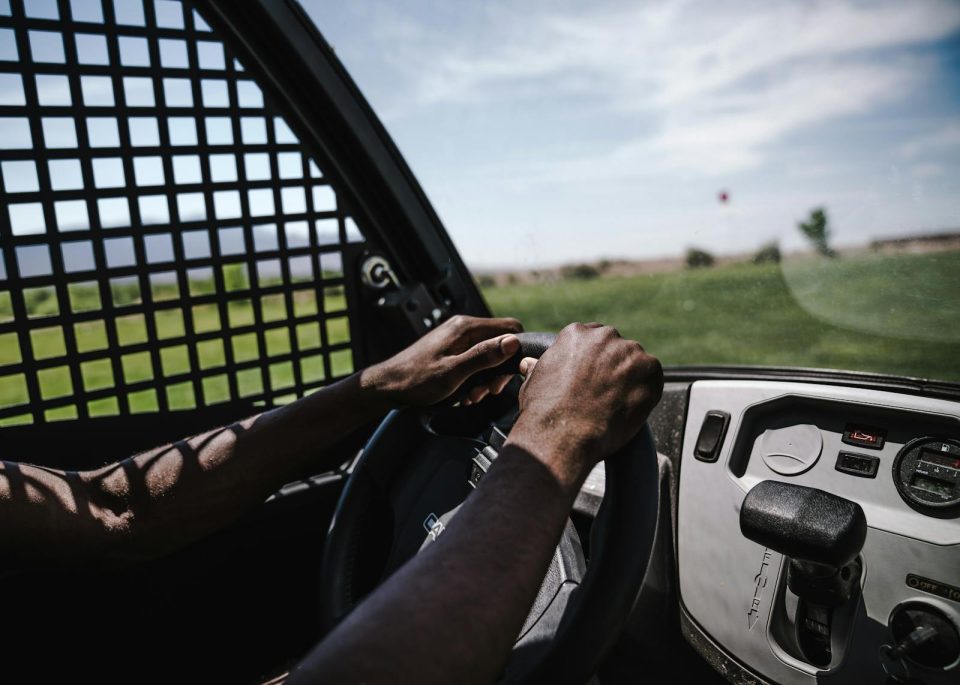 A close-up view of a person driving a golf cart in an outdoor setting with green fields visible.