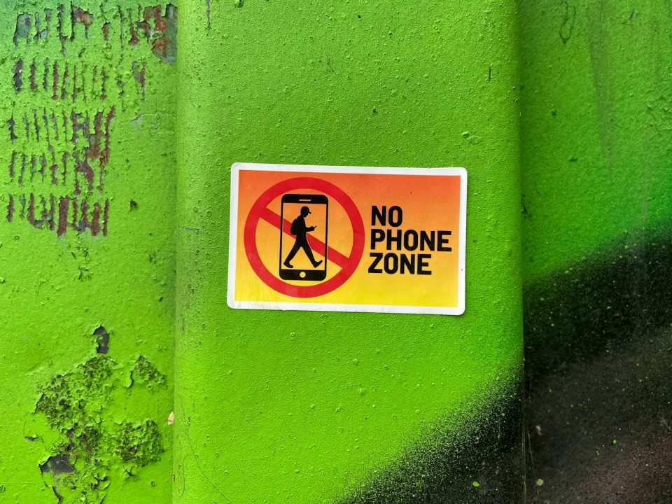 A no phone zone sign on a green wall