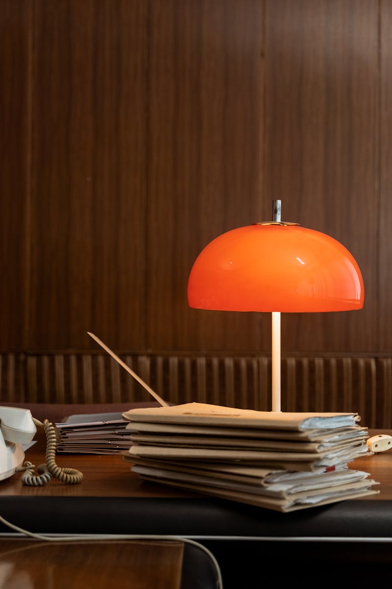 Retro office setting with a red lamp and stacked folders on a wooden desk, capturing a vintage vibe.