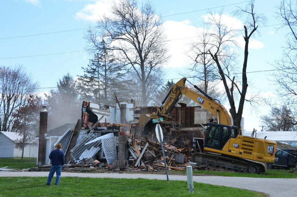 A house is being demolished by a backhoe.