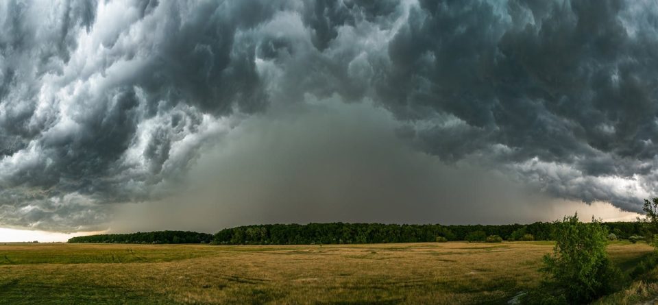 A dramatic thunderstorm rolls over a vast countryside field, creating an intense and moody atmosphere.