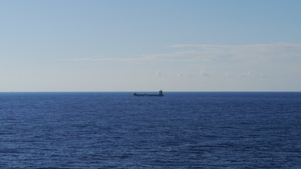 A tranquil scene of a bulk carrier ship cruising across a vast, open ocean under a clear blue sky.