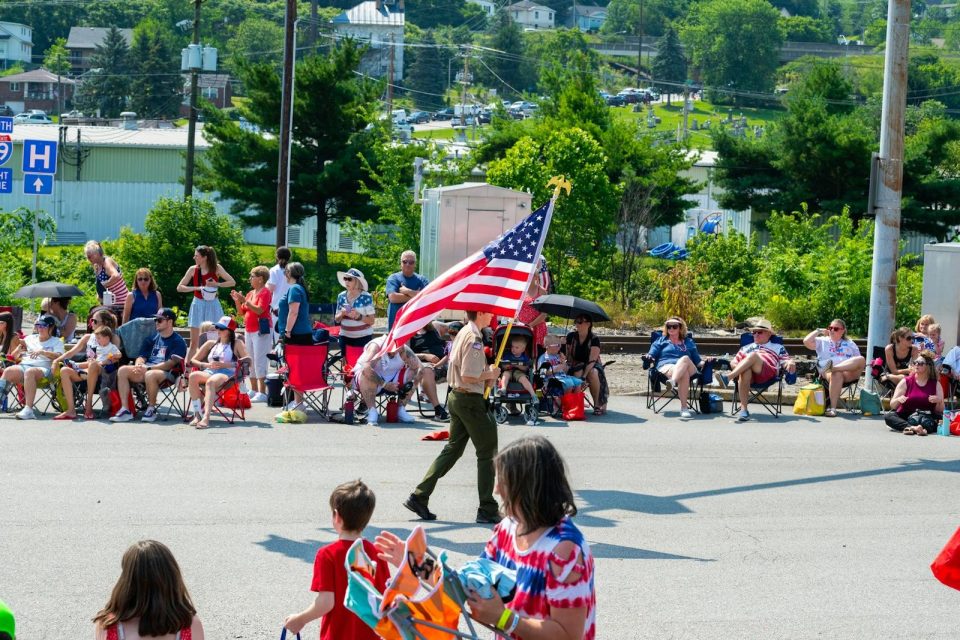 Boy Scout proudly carries the American flag during a community parade in a suburban area.