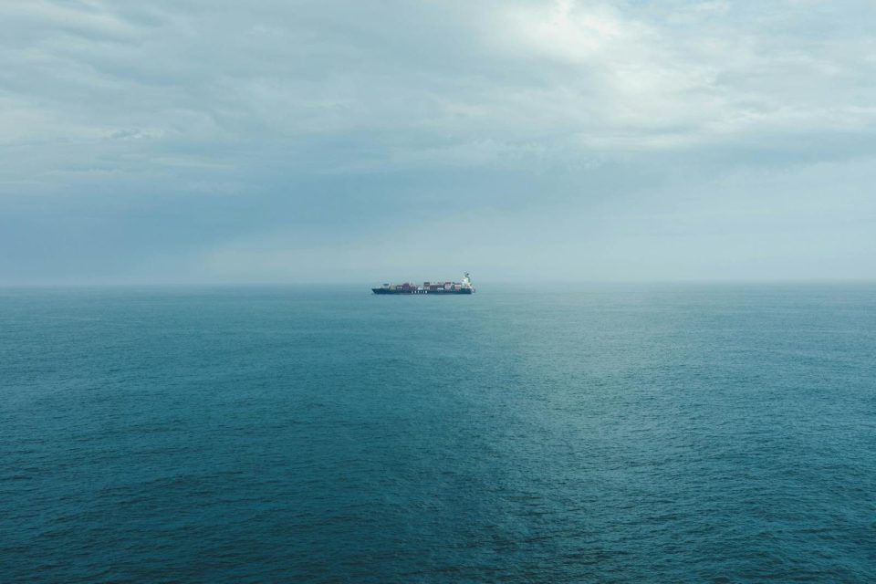 A lone cargo ship sails on a vast, calm ocean under a cloudy sky, depicting serenity and solitude.