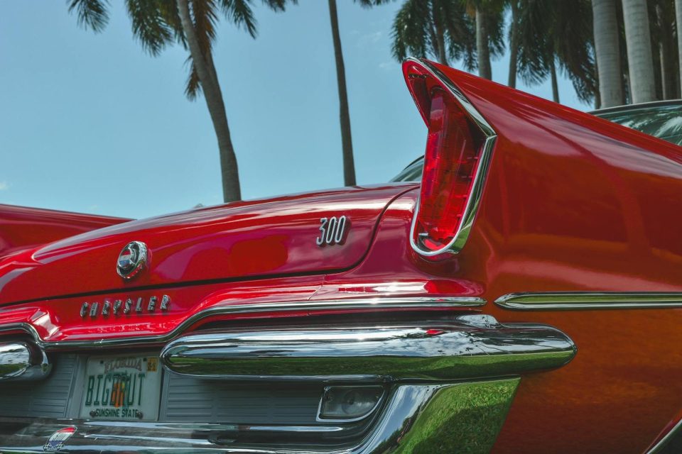 Vintage Chrysler 300 in red with palm trees, showcasing classic tail fin design with a sunny backdrop.