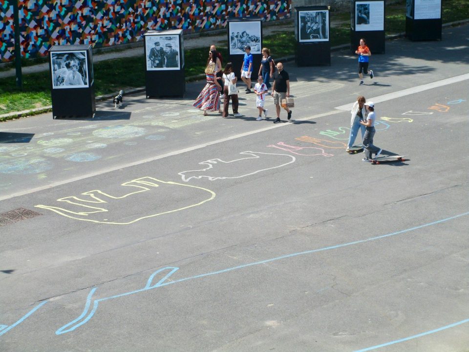 People strolling past outdoor photo exhibit and chalk drawings.