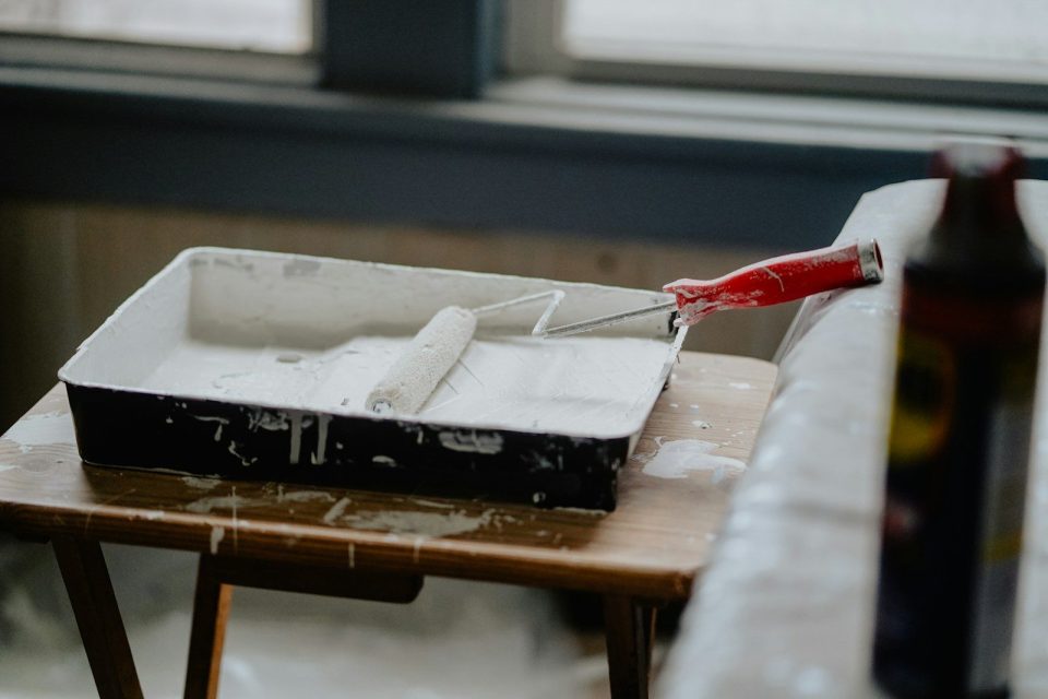 A paint roller with a red handle in a tray of white paint