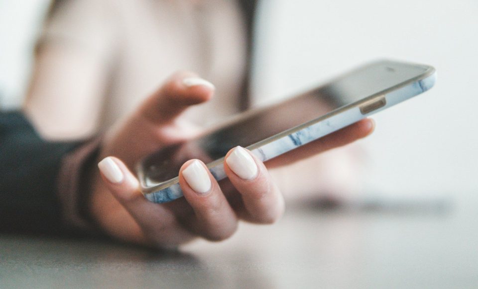 A person holding a smartphone with a marble pattern case in a bright room