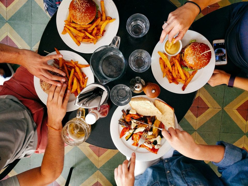 People eating burgers, fries, and roasted vegetables at a round table